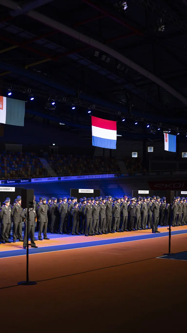 Militairen in dagelijks tenue staan naast elkaar opgesteld in een grote hal tijdens medaille-uitreiking.