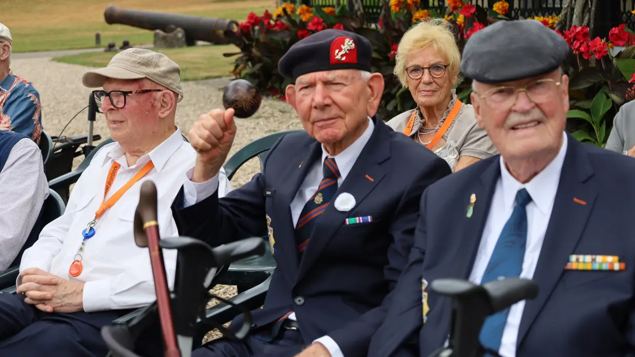 Alt: Drie oudere veteranen zitten buiten op het landgoed van Bronbeek naast elkaar. 