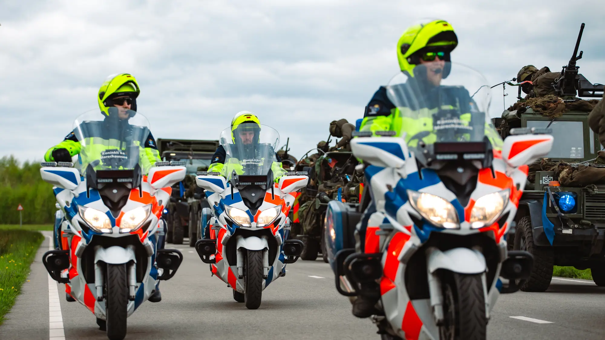 Motoren marechaussee rijden naast militaire voertuigen.