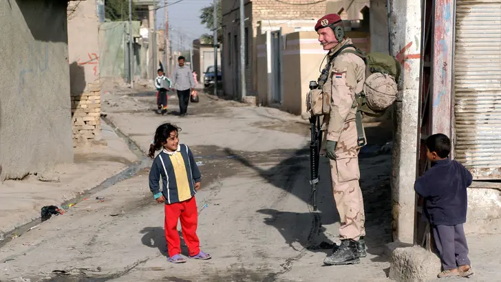 Infanterist lacht bij een klein meisje op straat in Irak.