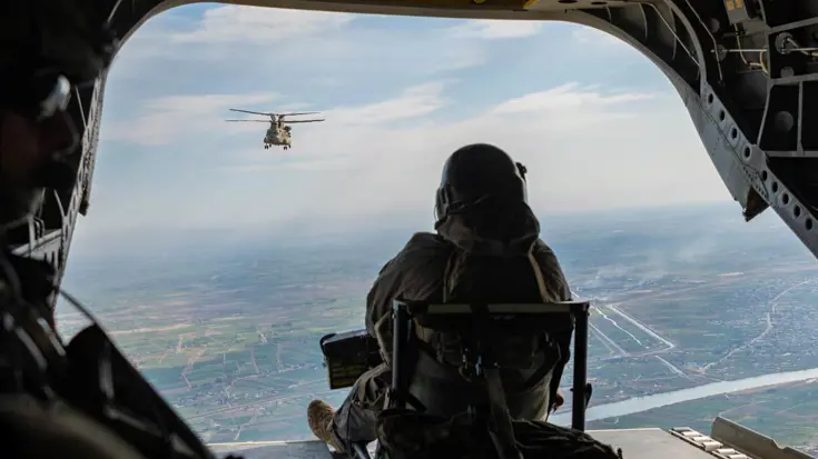 Een militair op de rug gezien. Hij zit in de open laadklep van een vliegtuig.