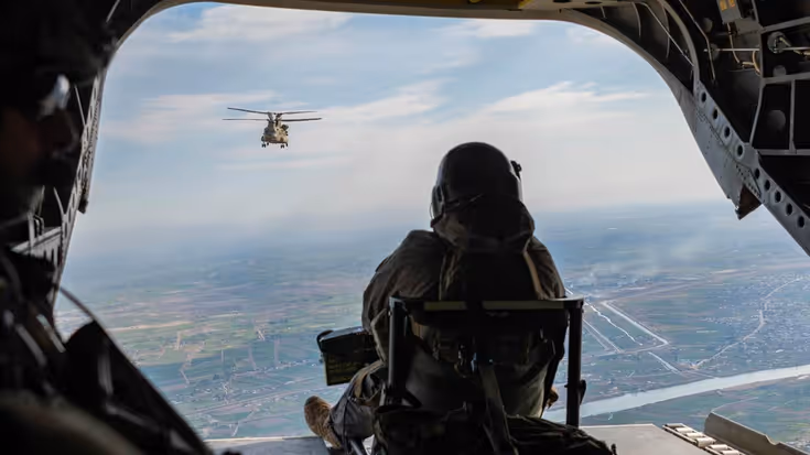 Een militair op de rug gezien. Hij zit in de open laadklep van een vliegtuig.