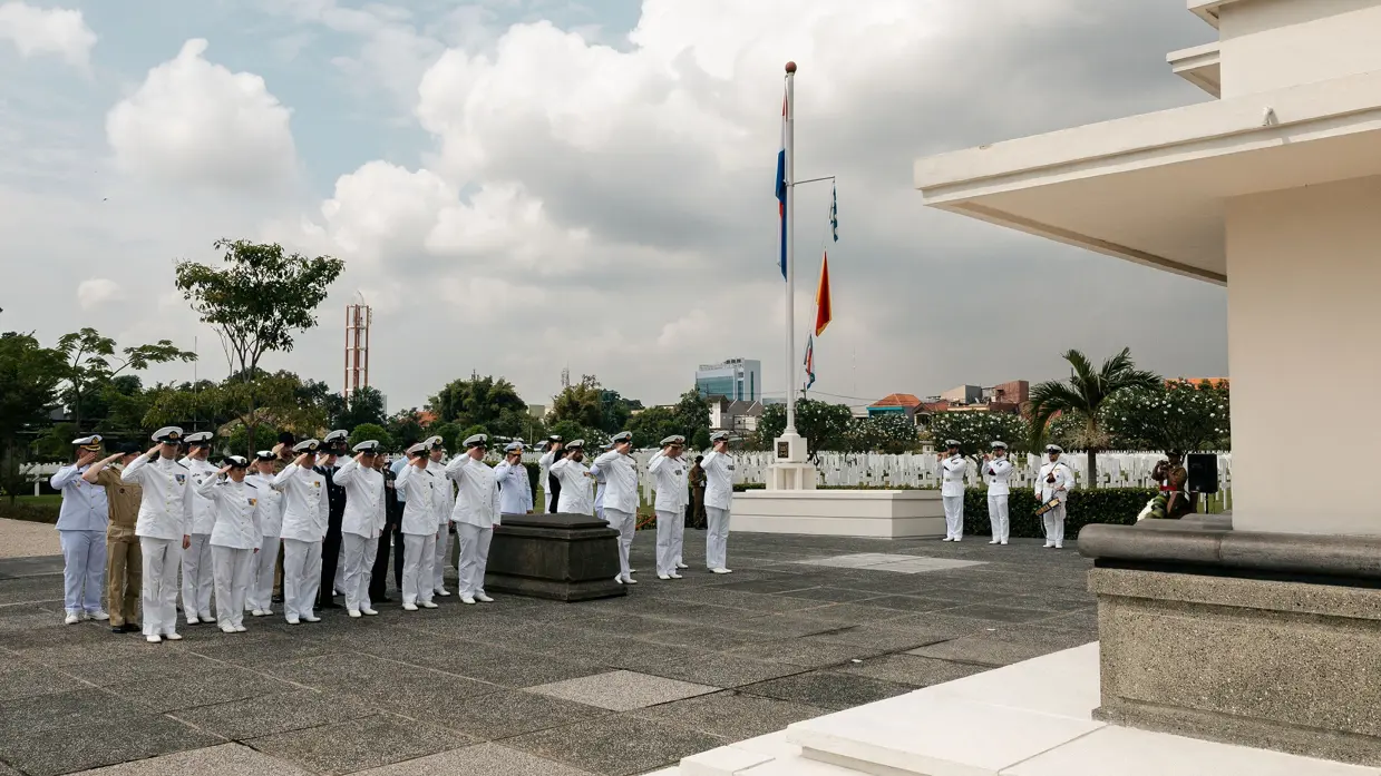 Een groep militairen saluteren bij een gedenkingsprocessie.