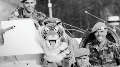 Twee militairen kijken in de camera. Er staat een pluche tijger tussen hen in.