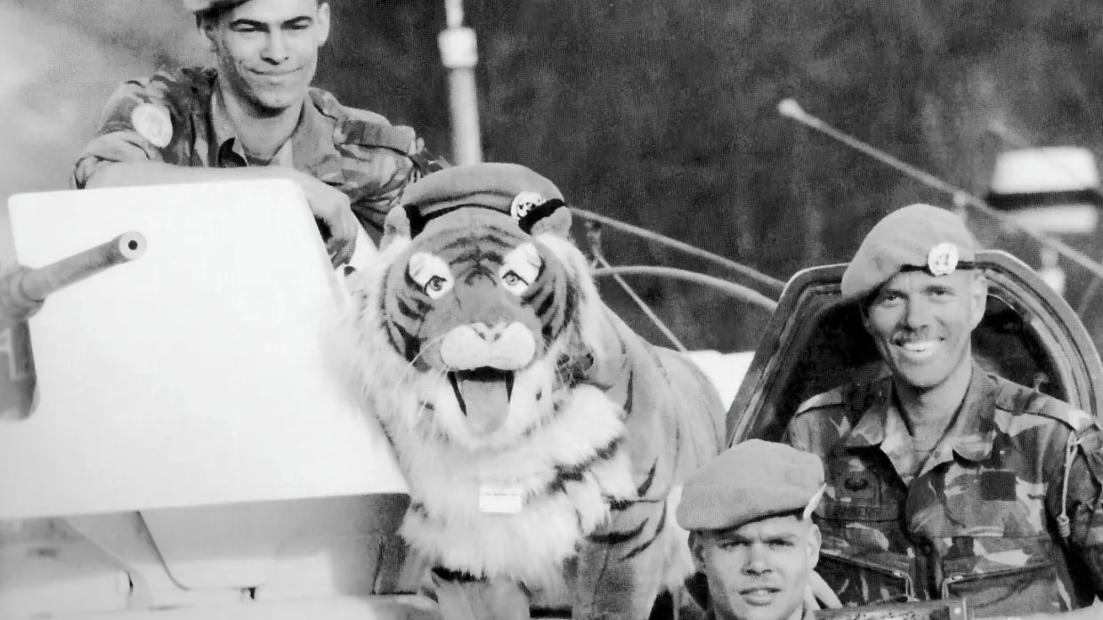 Twee militairen kijken in de camera. Er staat een pluche tijger tussen hen in.