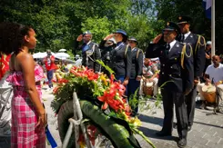 Militairen van het Multicultureel Netwerk Defensie salueren bij het Nationaal Monument Slavernijverleden. Een krans met bloemen op de voorgrond.