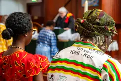 Twee bezoekers van Keti Koti in kleurige kleding zittend vanaf de rug gezien.