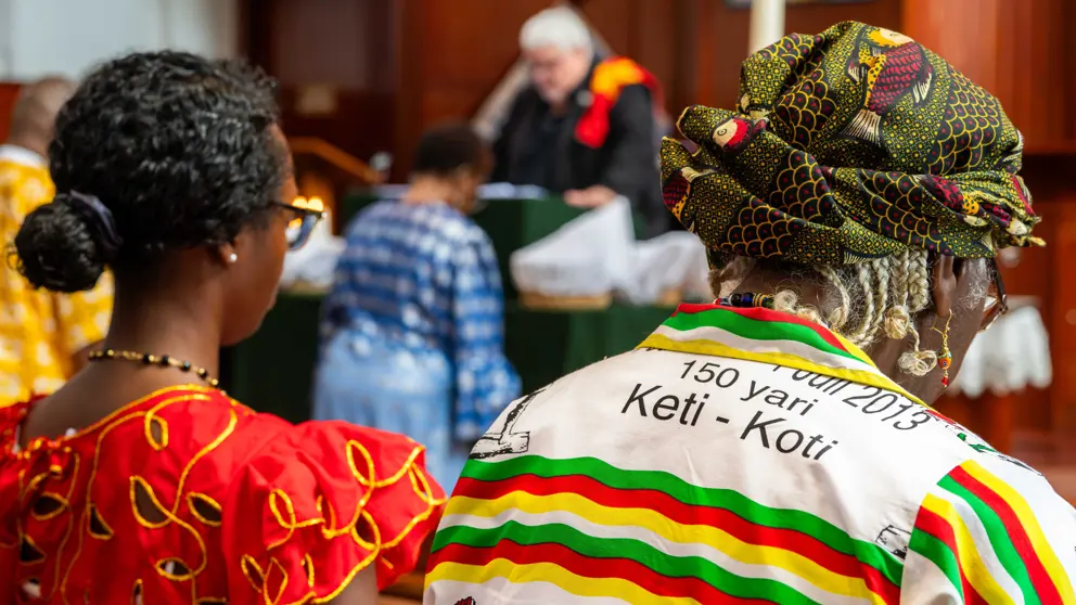 Twee bezoekers van Keti Koti in kleurige kleding zittend vanaf de rug gezien.
