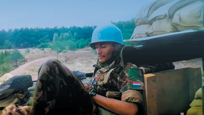 Een militair met een blauwe helm is iets aan het lezen op een berg, omgeven door zandzakken.