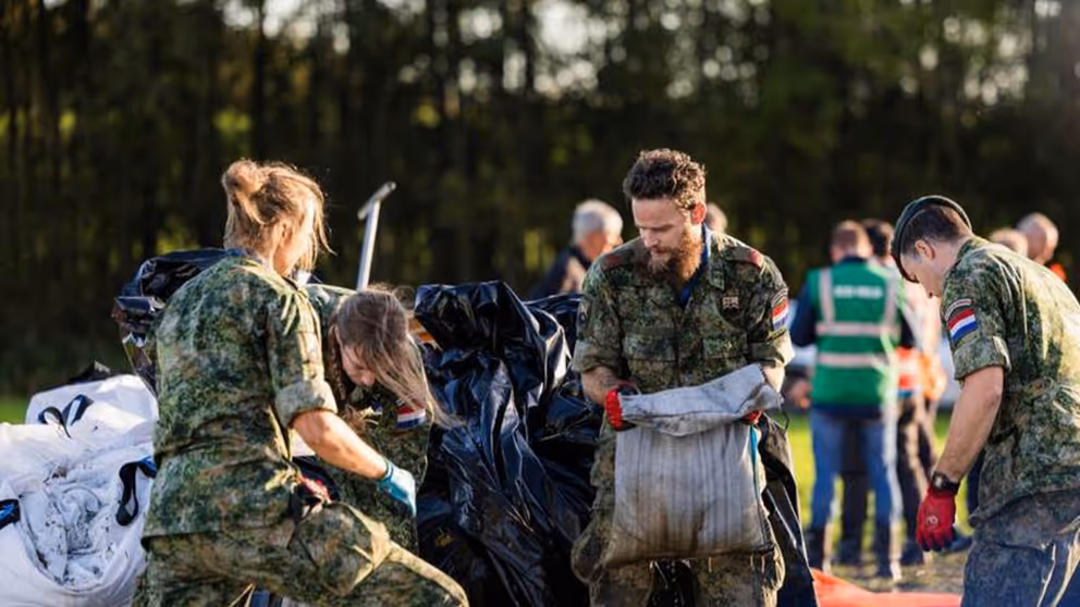 Mannelijke  en vrouwelijke militairen zijn bezig met zandzakken.