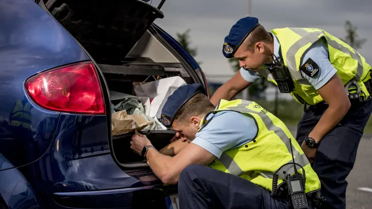 2 marechaussees onderzoeken de achterbak van een auto.