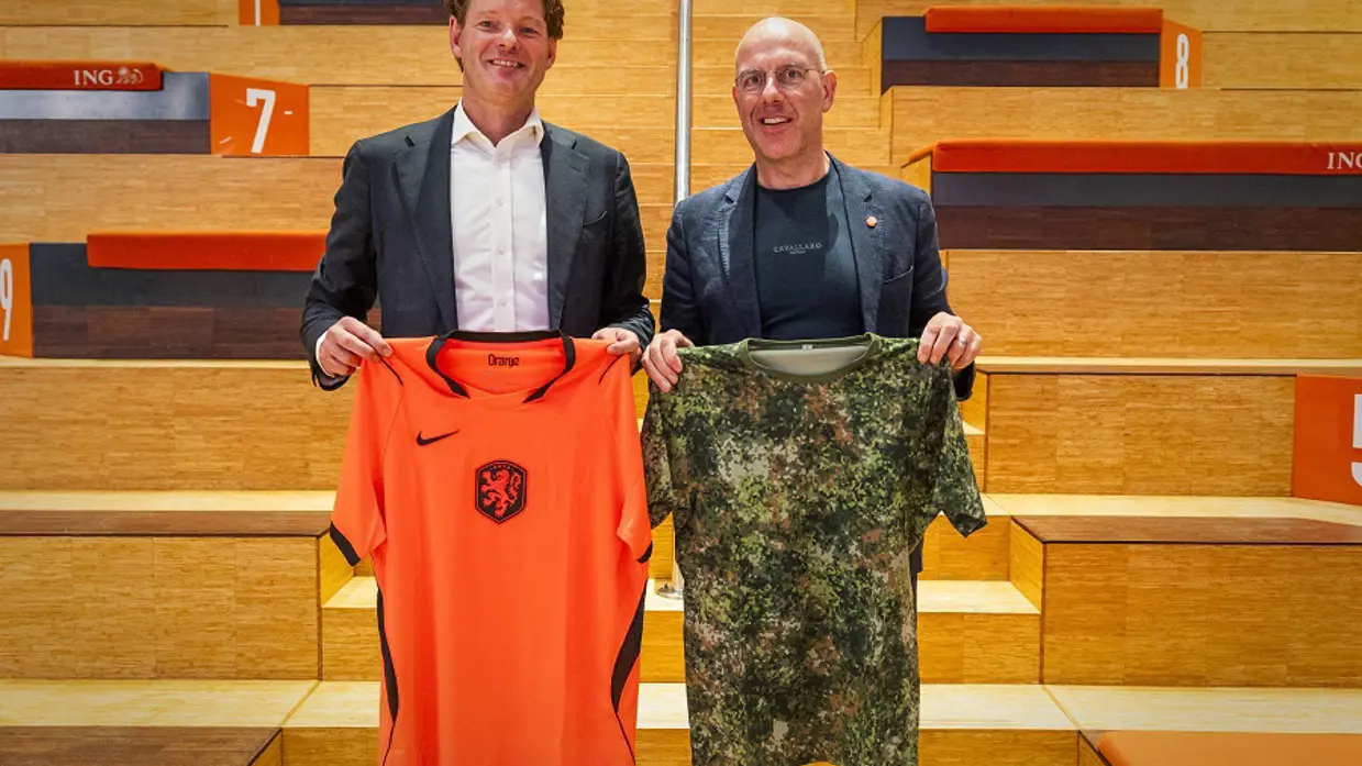Secretaris-generaal van Defensie Maarten Schurink en secretaris-generaal van de KNVB Gijs de Jong poseren met een voetbalshirt en een Defensie-shirt