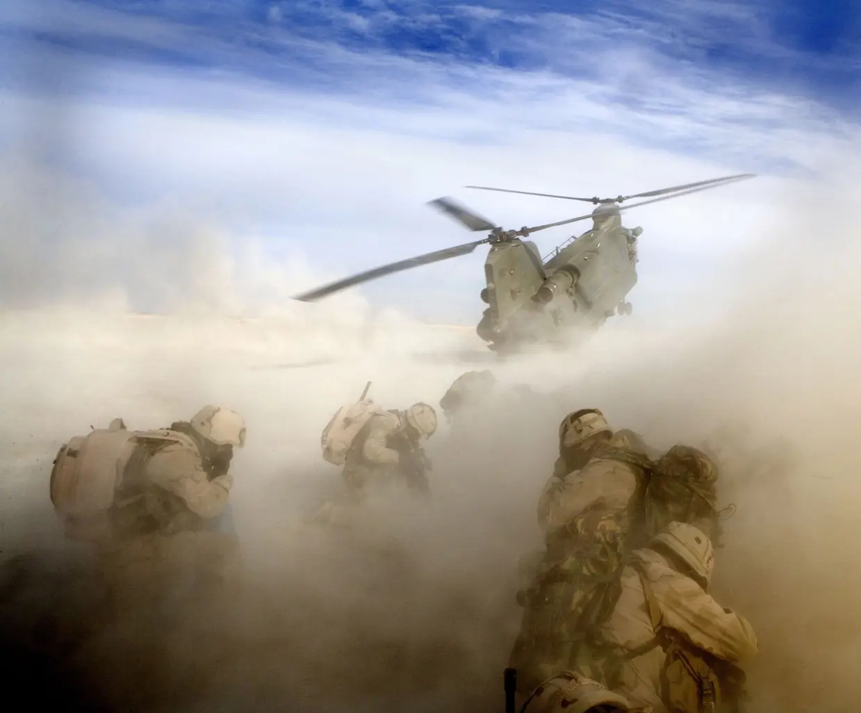 Een Chinook-helikopter stijgt op en maakt stofwolk om militairen.