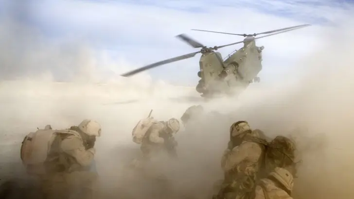 Een Chinook-helikopter stijgt op en maakt stofwolk om militairen.