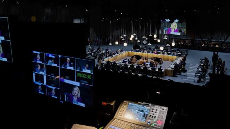 Grote vergadertafel met schermen op voorgrond. 