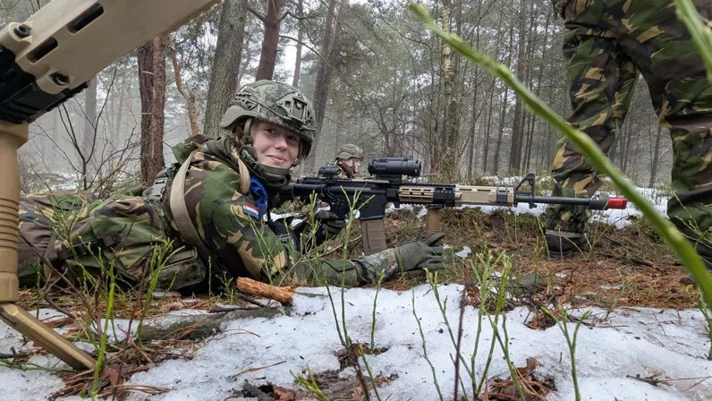 Floor ligt tijdens een militaire oefening in een besneeuwd bos in camouflage-uniform met een oefenwapen in haar handen.