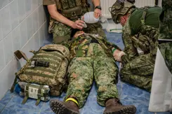 Gewonde militair ligt op zijn rug op de grond. Hij wordt behandeld.