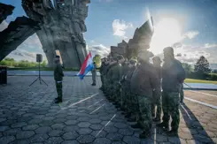 Militairen staan in de houding terwijl een van hen de Nederlandse vlag vasthoudt.