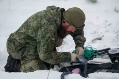 Militair op knieen in de sneeuw bezig met bevestiging van draden.