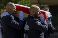 Militairen dragen kist met Nederlandse vlag tijdens herbegrafenis.