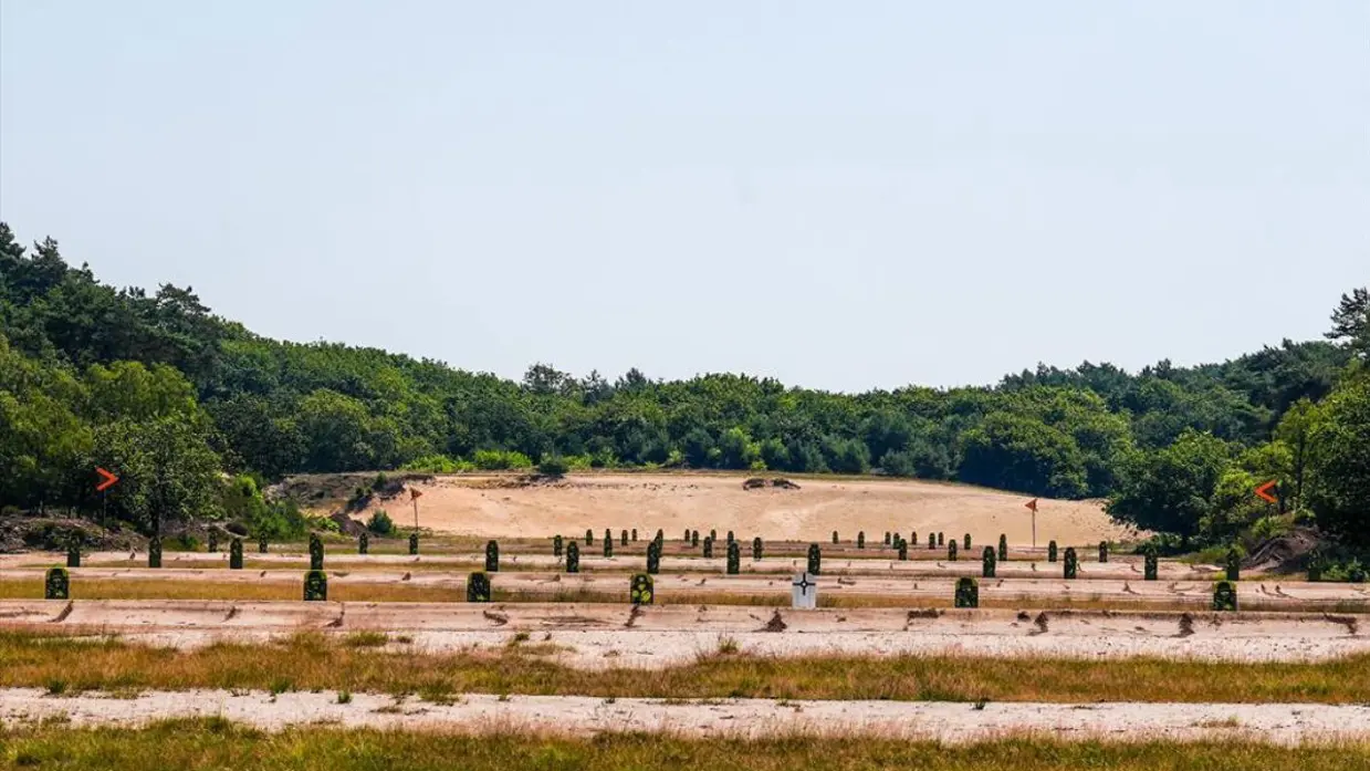 Een buitenschietbaan: een vrij open zandveld met aan de randen begroeiing. 