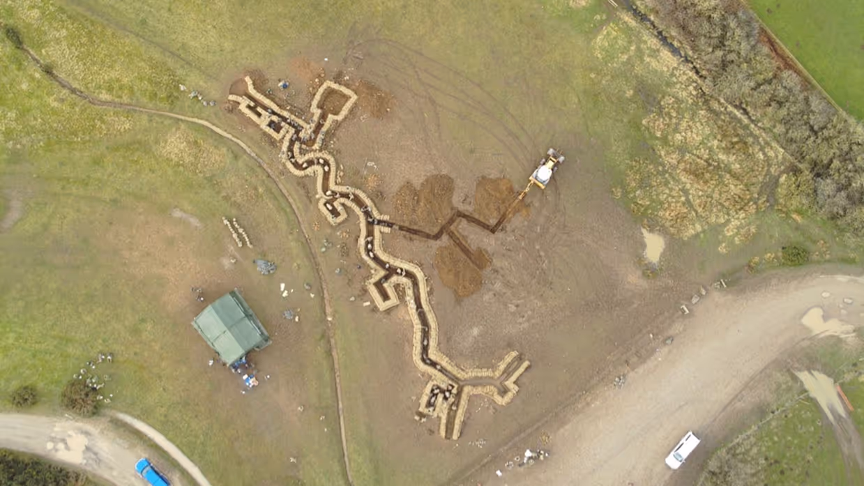 Links: Luchtfoto van loopgraven op militair oefenterrein. Rechts: Militair met wapen hurkt in loopgraaf waarvan de wanden met golfplaten zijn bekleed. Op zijn helm een bos stro als camouflage.