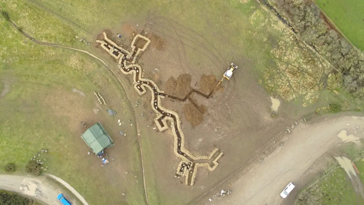 Links: Luchtfoto van loopgraven op militair oefenterrein. Rechts: Militair met wapen hurkt in loopgraaf waarvan de wanden met golfplaten zijn bekleed. Op zijn helm een bos stro als camouflage.