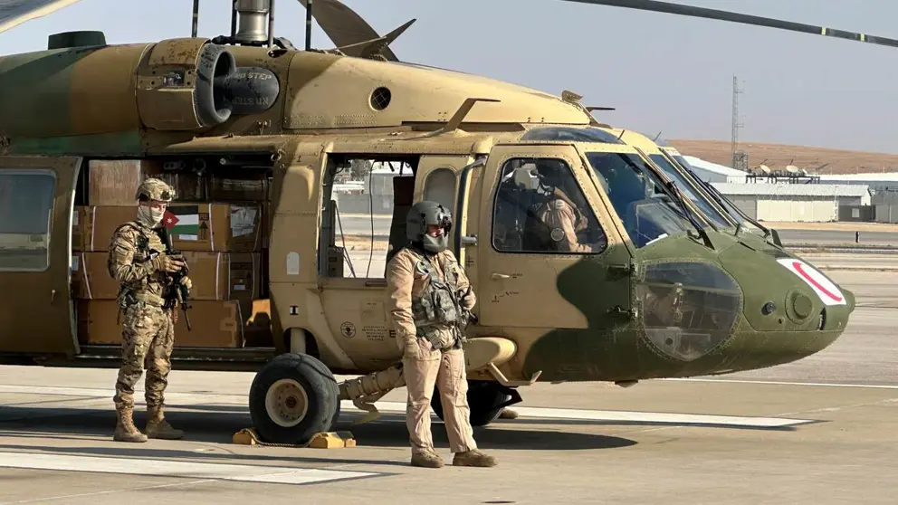 Dozen met hulpgoederen staan in een helikopter met de deur open. 2 militairen staan naast de helikopter..