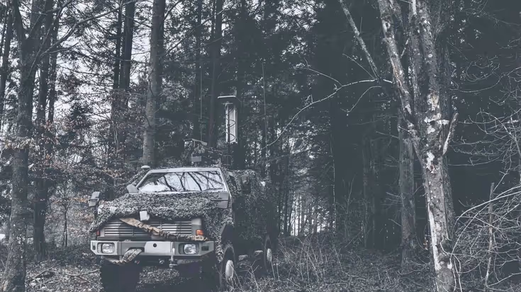 Jeep met camouflage net in het bos.