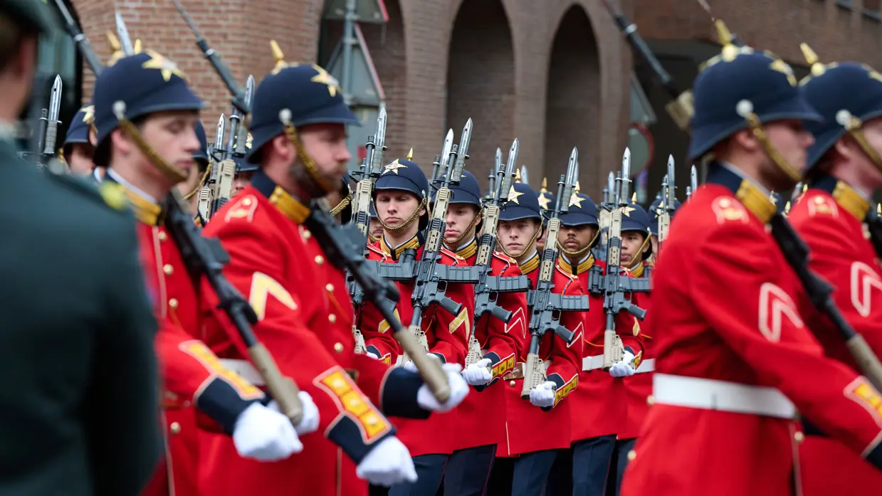 Marcherende militairen in rode jasjes.