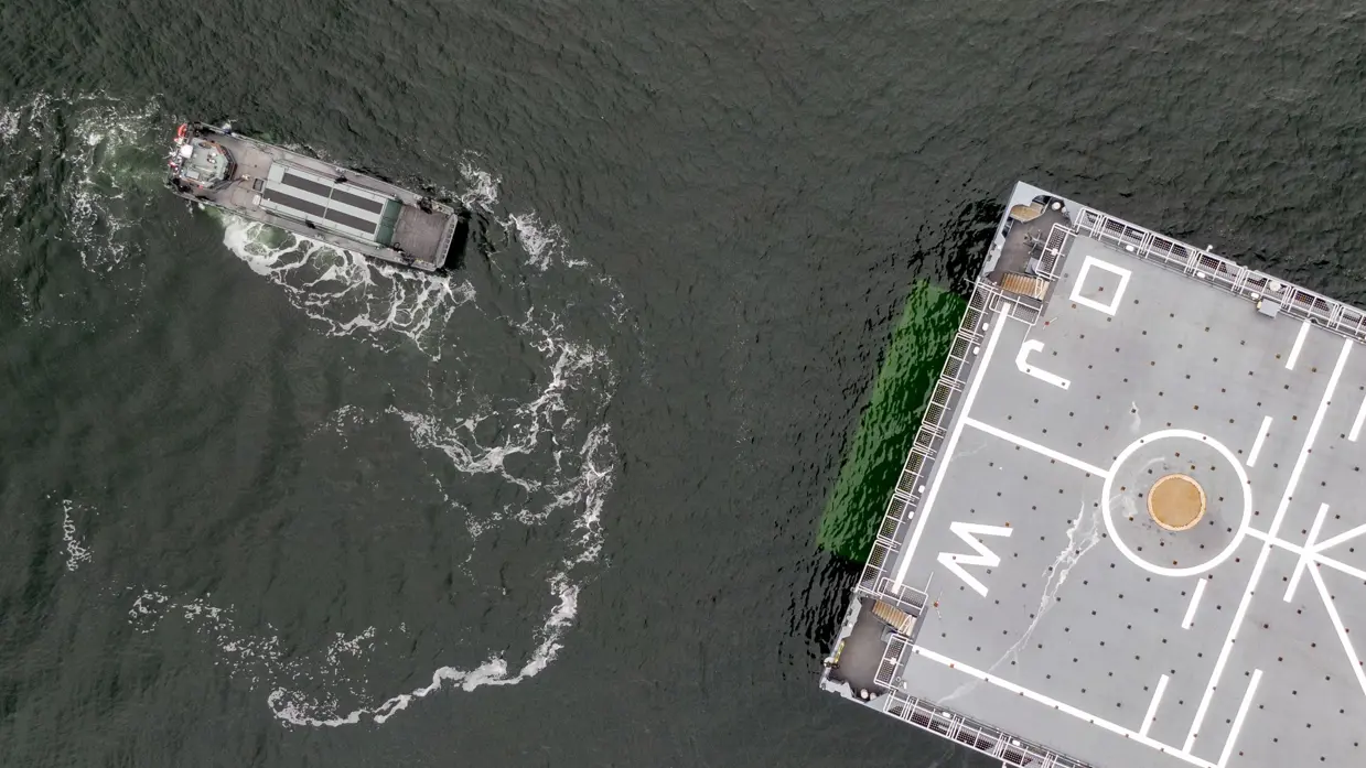 Kleine boot van bovenaf gezien. Dek groot marineschip half in beeld.