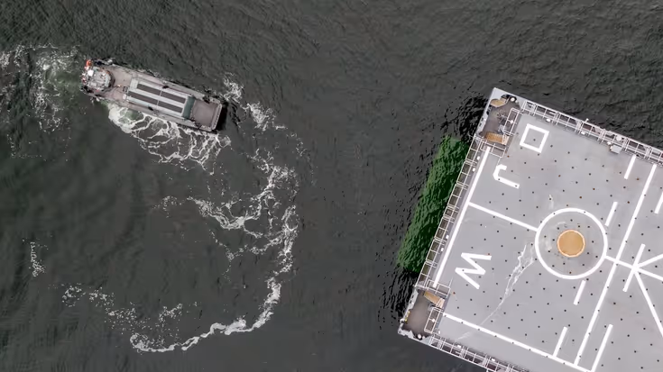 Kleine boot van bovenaf gezien. Dek groot marineschip half in beeld.