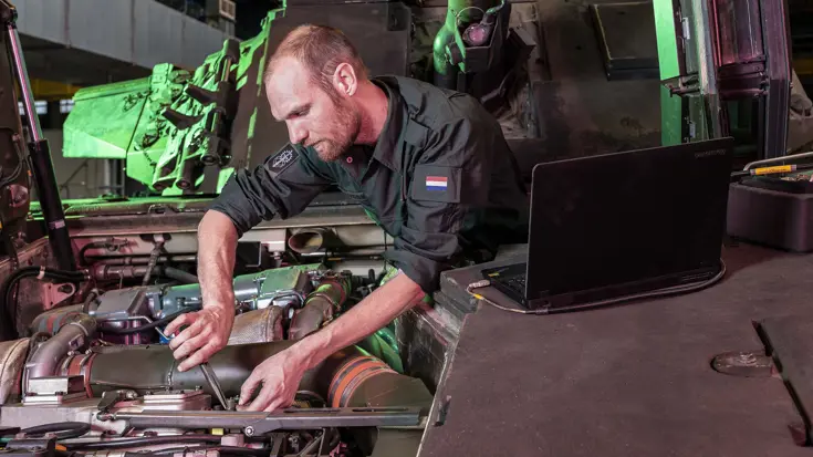 Een militair bezig met de motor aan een voertuig.