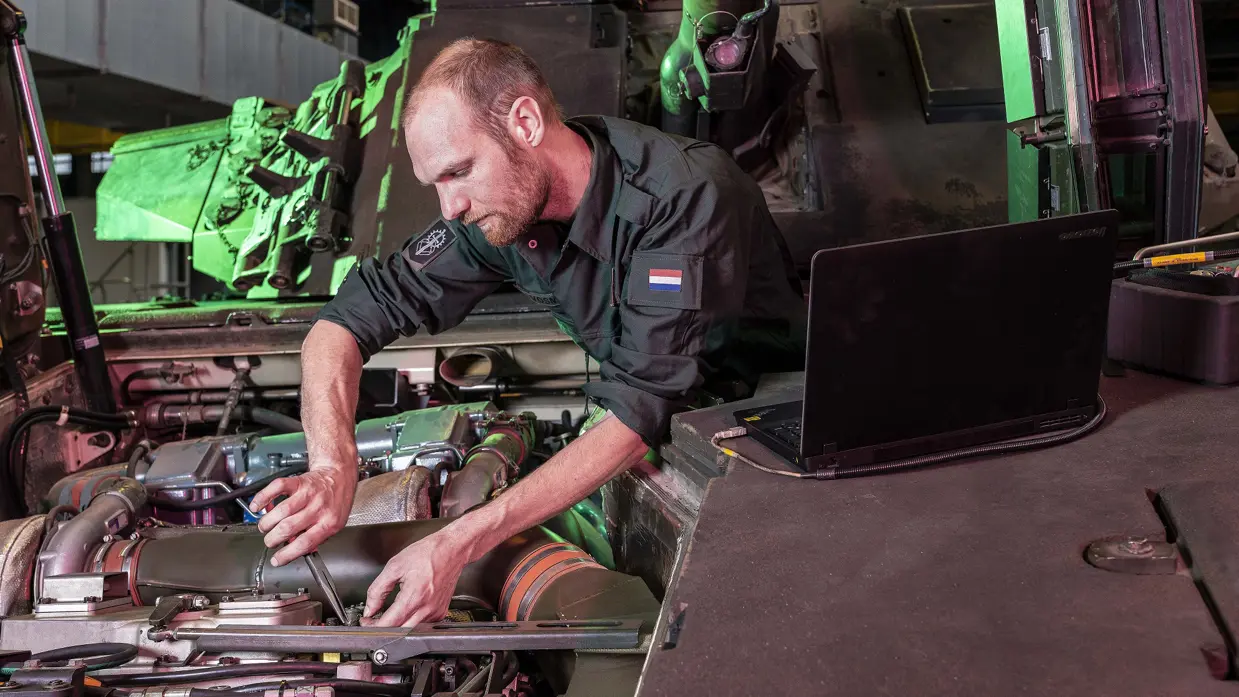 Een militair bezig met de motor aan een voertuig.