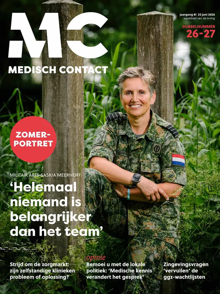 De cover van Medisch Contact toont een glimlachende militair arts in camouflagekleding, zittend tussen groene planten en houten palen.