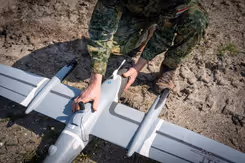 Gehurkte militair werkt aan drone die op de grond ligt.