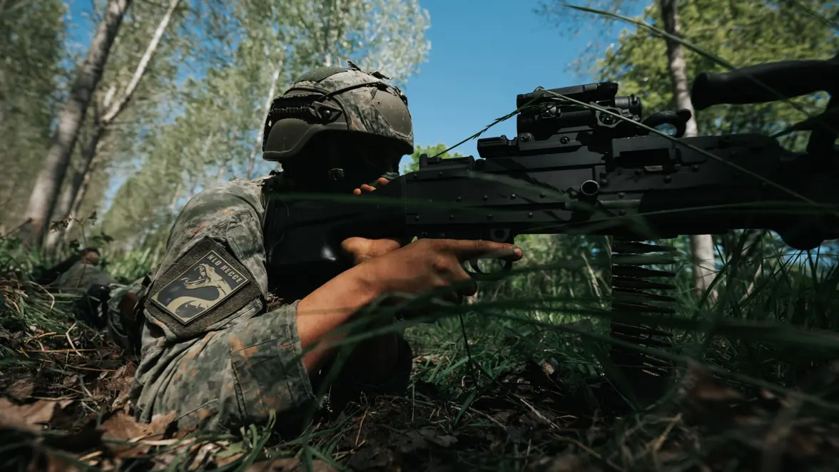 Een militair ligt op de grond met een vuurwapen in zijn handen. 