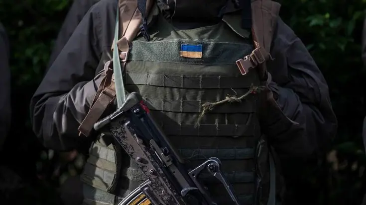 Vest van militair met Oekraïense vlag erop. Voor de borst hangt een machinegeweer.