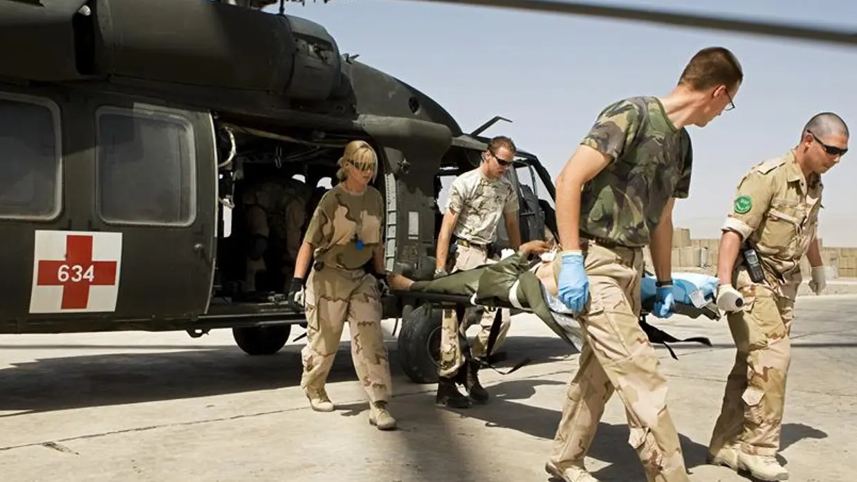 Militairen vervoeren per brancard een patiënt uit een helikopter.
