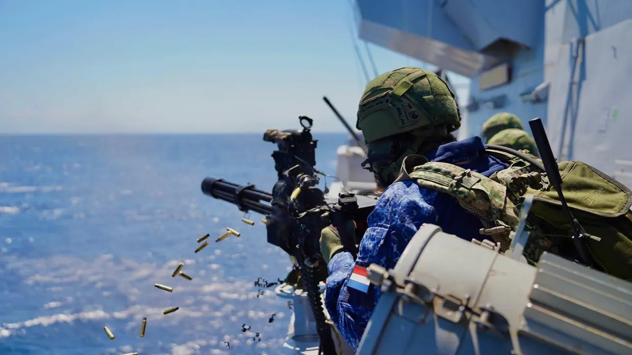 Een militair schiet vanaf het schip met een minigun op het water.