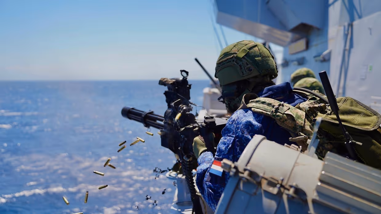 Een militair schiet vanaf het schip met een minigun op het water.