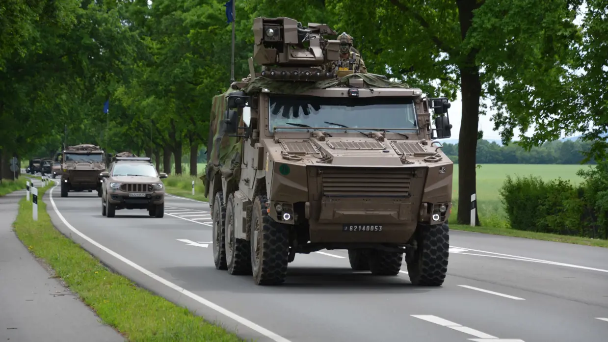 Militaire pantserwagens rijden op een landweg tussen bomen en andere voertuigen.