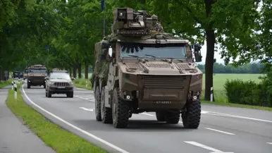 Militaire pantserwagens rijden op een landweg tussen bomen en andere voertuigen.