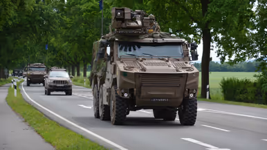 Militaire pantserwagens rijden op een landweg tussen bomen en andere voertuigen.