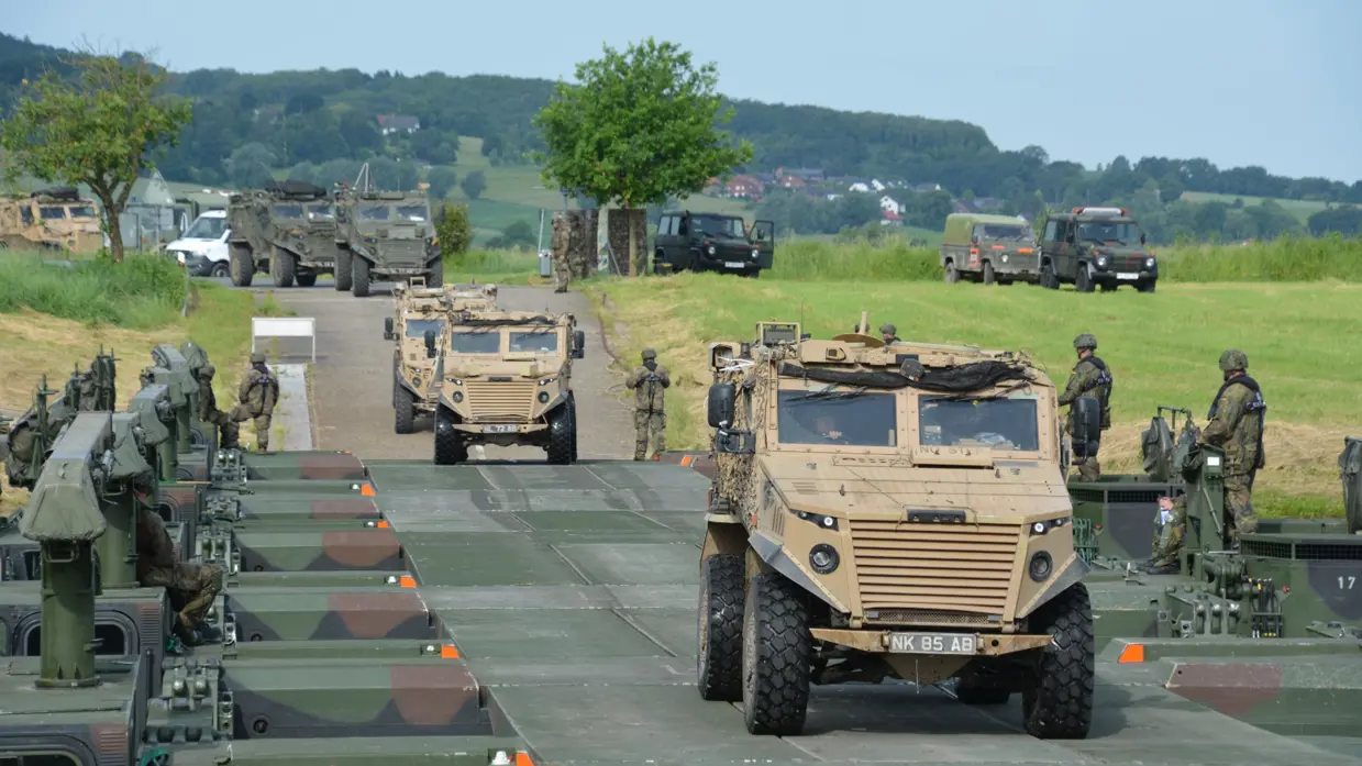 Militaire pantserwagens rijden op een landweg tussen bomen en andere voertuigen.