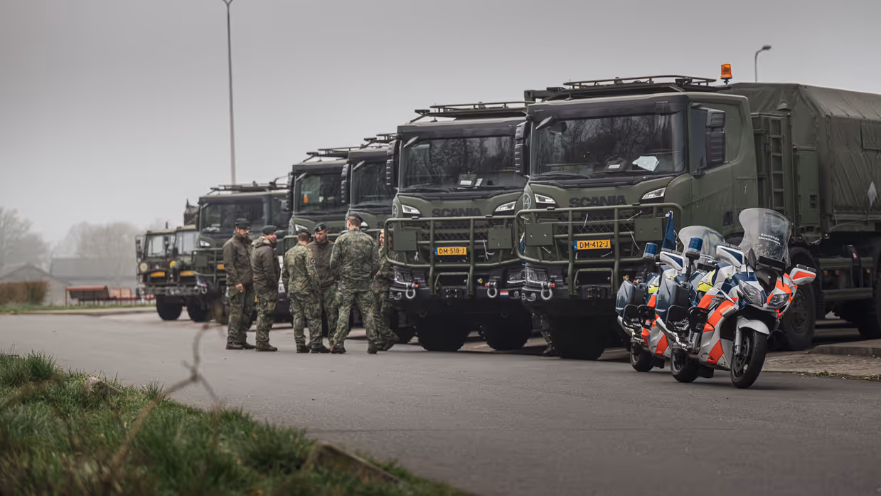 Militaire Scania-vrachtwagens met personeel en marechausseemotoren ervoor.
