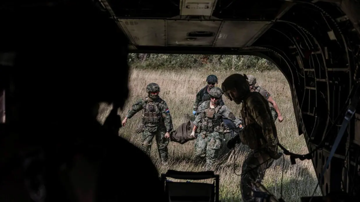 Militairen lopen met brancard naar ambulance. Foto gemaakt vanuit de ambu.