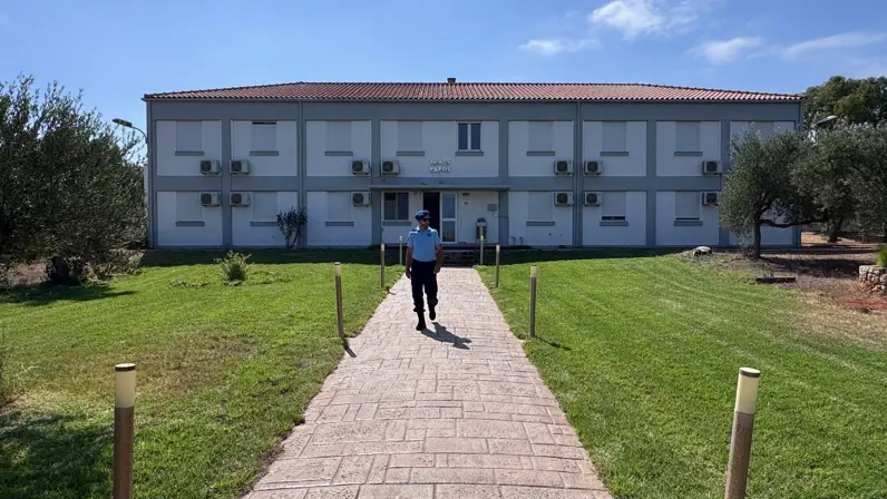 Een marechaussee loopt voor een betonnen barak met Griekse letters boven de ingang.