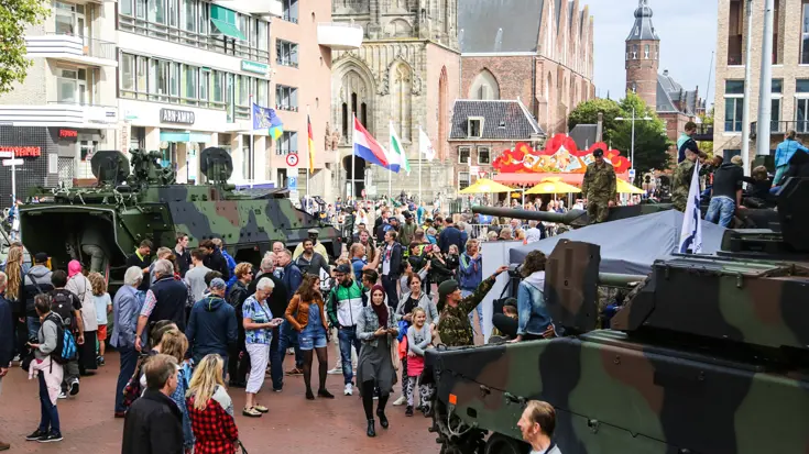 Landmachtvoertuigen tussen publiek in straten tijdens open dag.