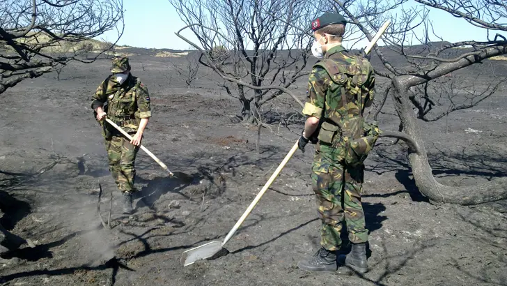Militairen Korps Nationale Reserve met schoppen helpen natuurbrand in duinen doven.